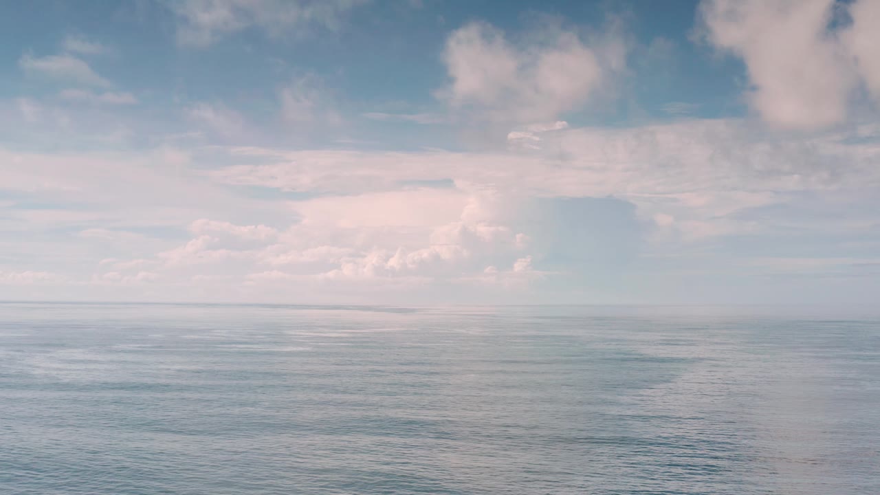 Open Los Cabos water remains centered below soft cloudy sky, with faint ripples across the ocean and no visible people.