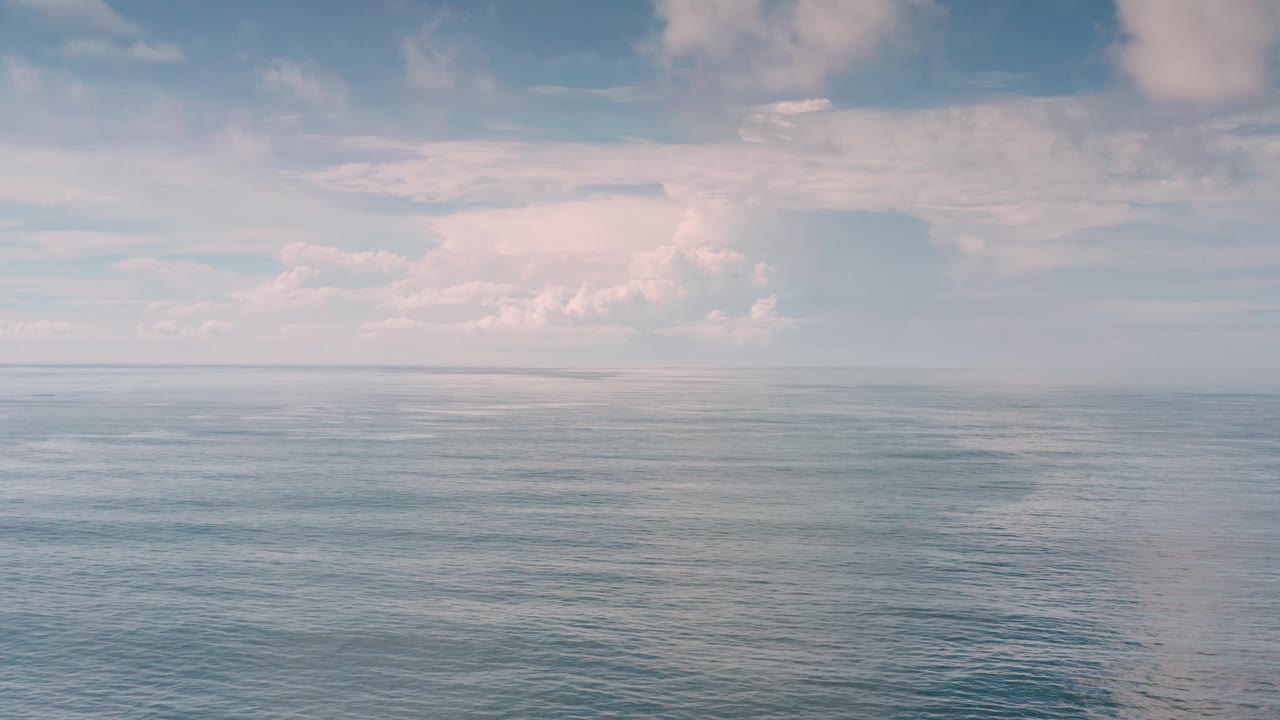 Open water stretches toward a low horizon in Los Cabos, Mexico, with larger pale clouds grouped above and no visible people.