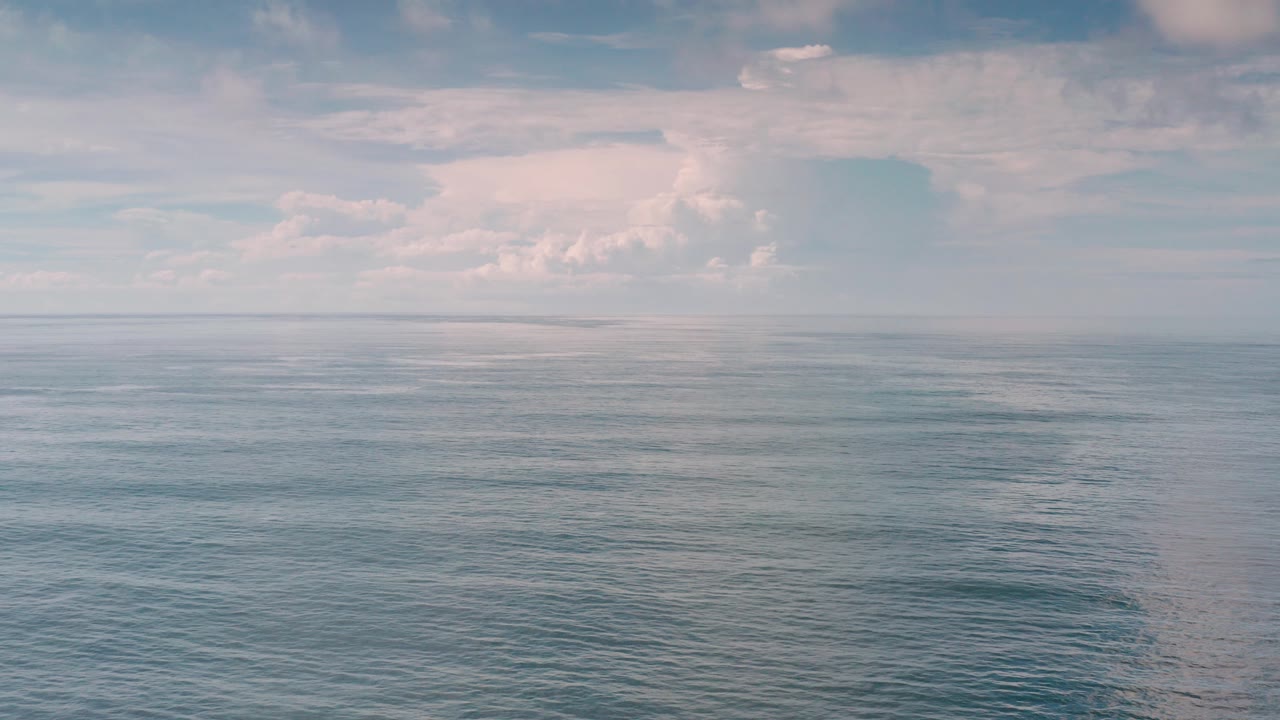 Wide ocean horizon with pale clouds and textured water