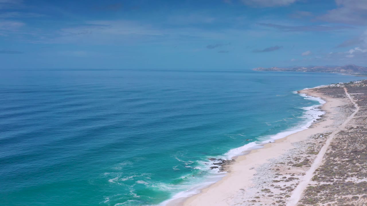 Open ocean bands approaching a pale beach under blue sky.