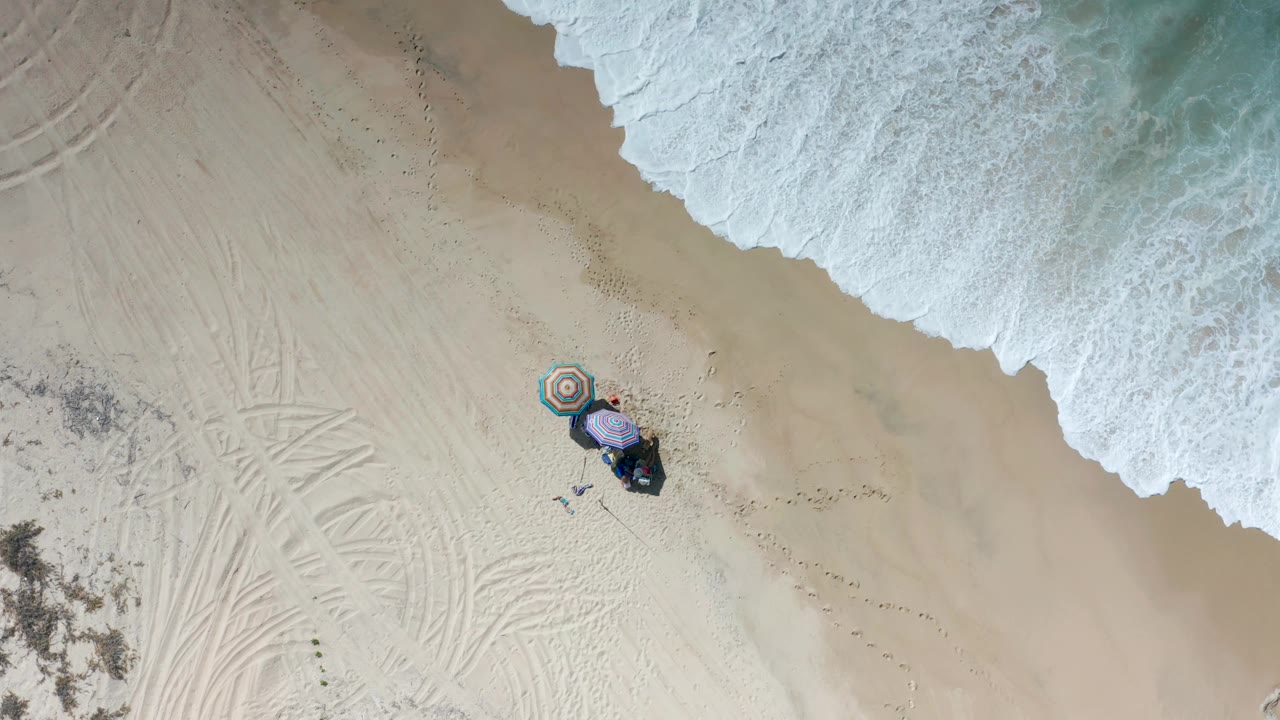 Top-down beach scene with umbrellas and waves along the upper shoreline.