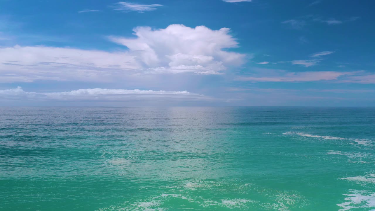 Los Cabos coastal water under a broad white cloud formation, with teal water in front, darker blue water near the horizon, and no visible people.