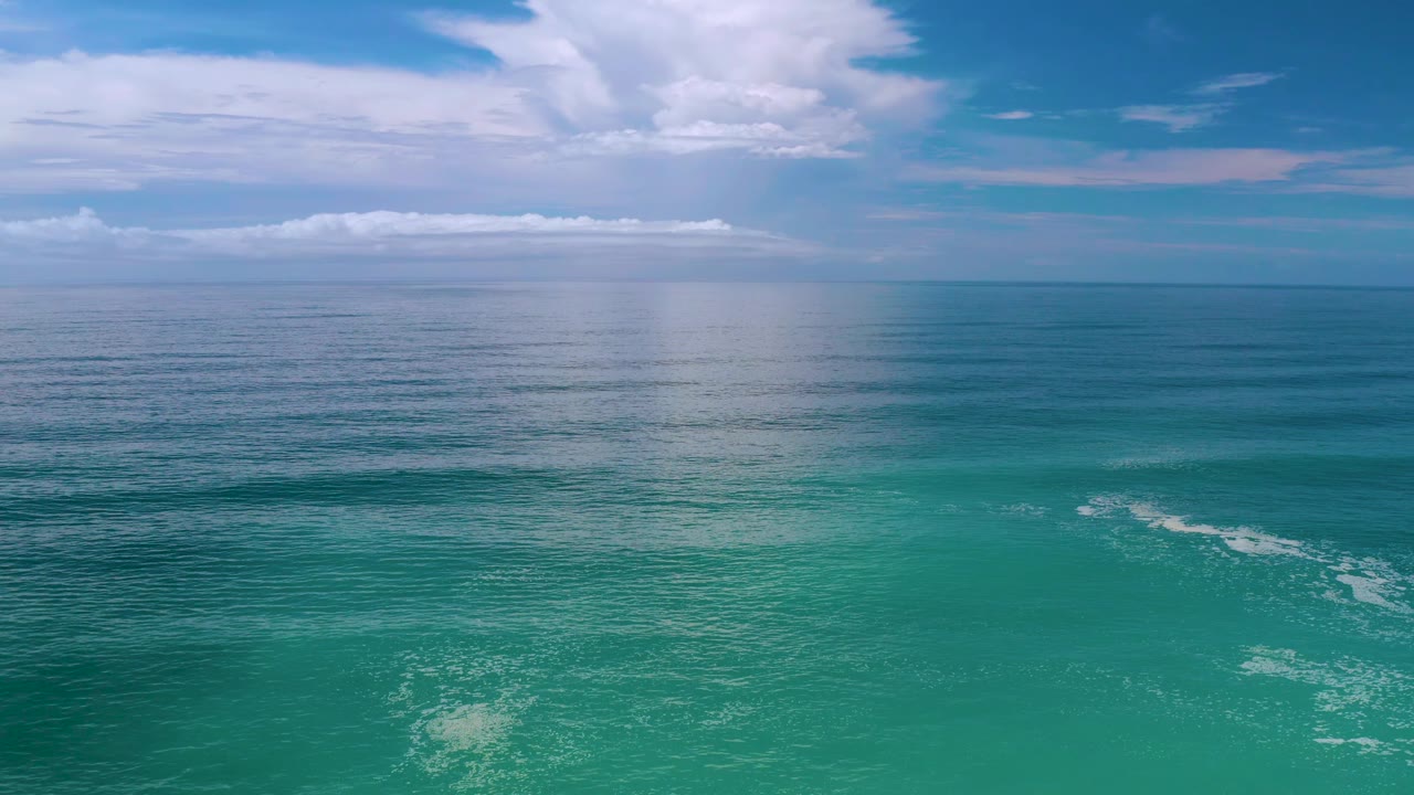 Los Cabos, Mexico ocean scene with green-blue water, thin wave texture near the lower right, layered white clouds, and no visible people.