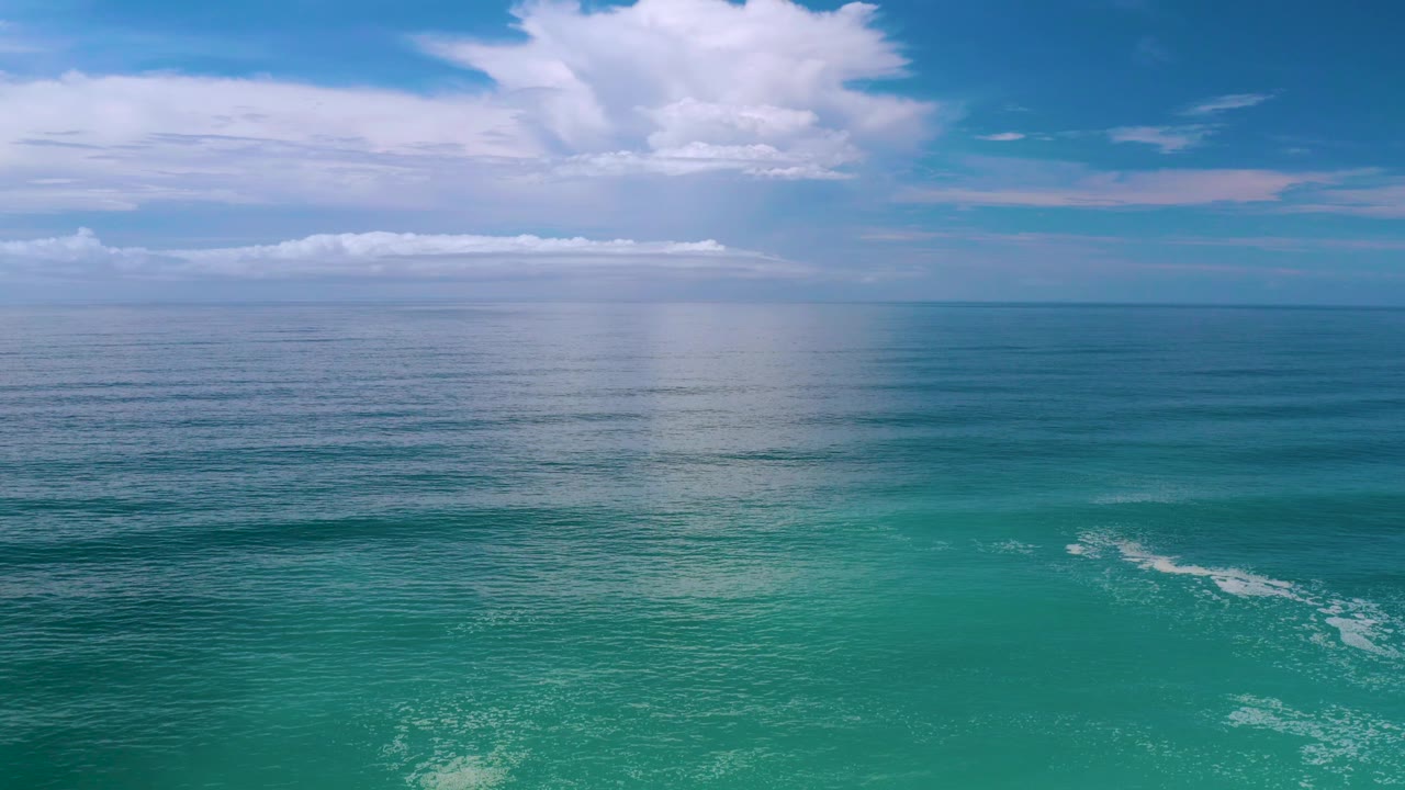 Los Cabos, Mexico horizon view where bright clouds mirror faintly on calm water, with turquoise foreground water and no visible people.