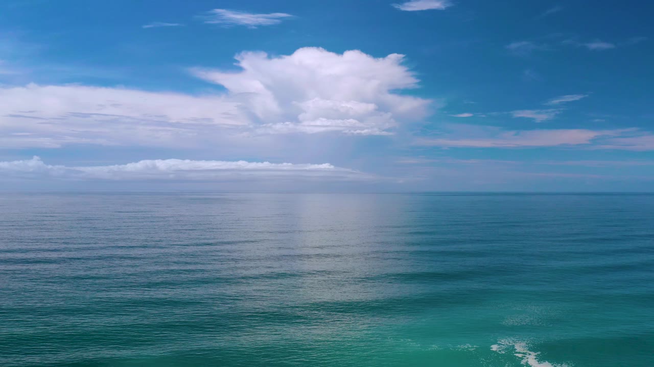 Open blue water fills the lower frame in Los Cabos, with layered white clouds and a clear horizon, and no visible people.