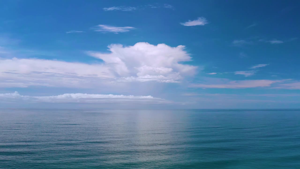 Los Cabos seascape with a broad white cloud centered above the horizon and a pale reflection falling across the water, with no visible people.