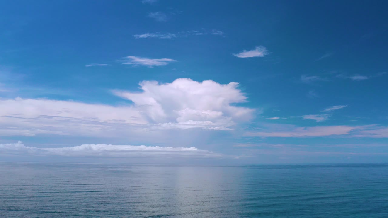 Opening view of the Los Cabos blue sea beneath layered white clouds and a bright sky, with no visible people.