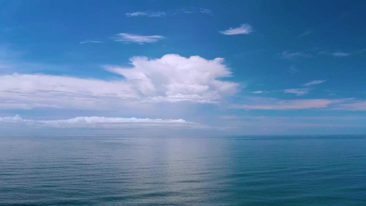 Los Cabos ocean frame with soft water ripples, a broad cloud reflection near center, layered white clouds on the horizon, and no visible people.