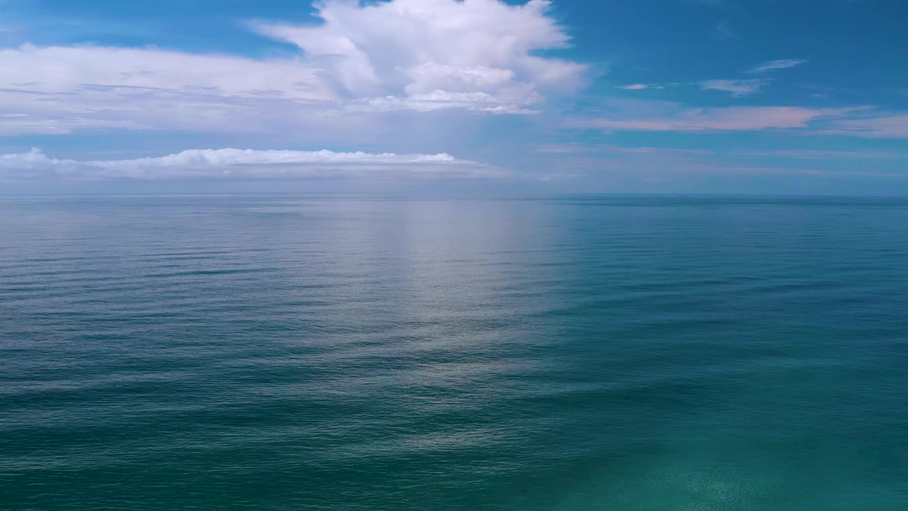Los Cabos, Mexico ocean surface with soft ripples in the foreground, a pale cloud reflection in the midwater, white clouds overhead, and no visible people.