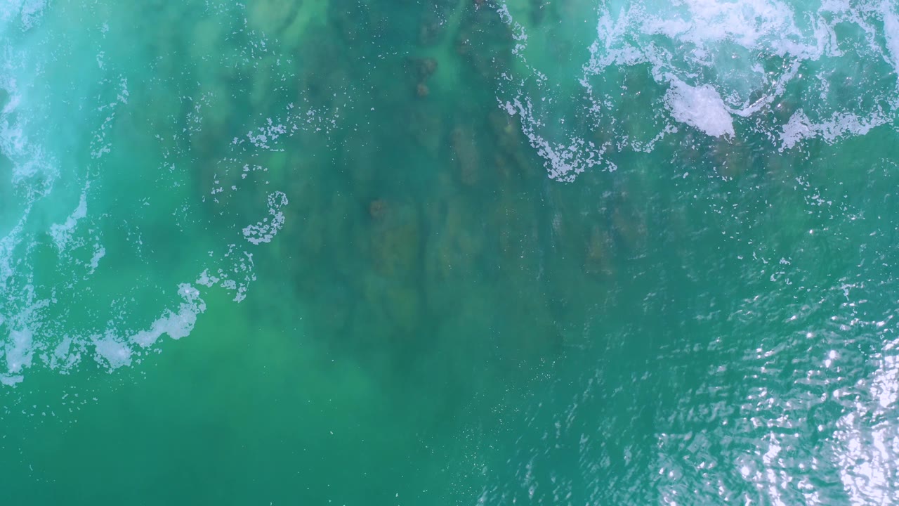 Overhead turquoise water in Los Cabos with breaking foam entering from the upper left, darker underwater patches visible through the surface, and no visible people.