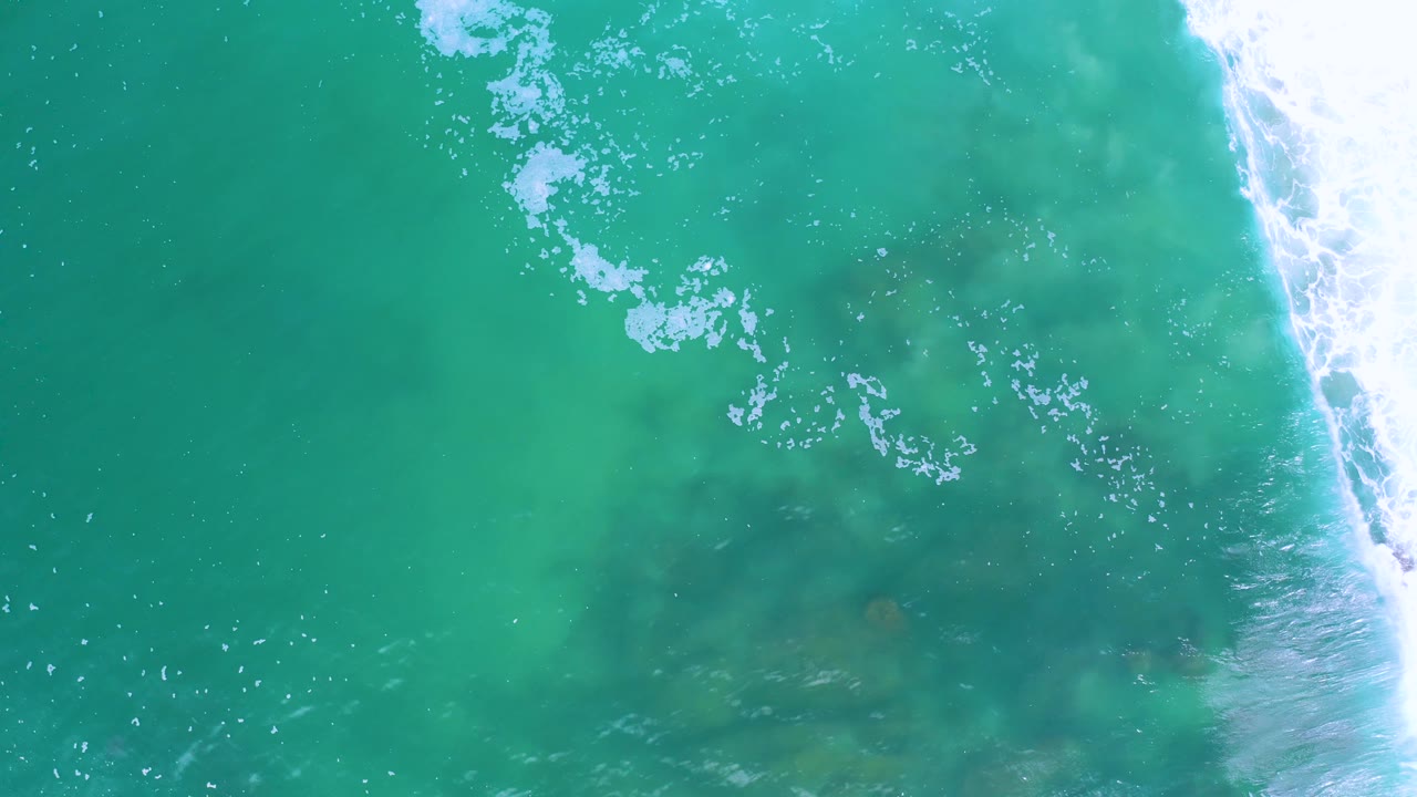 Top-down frame of green-blue water in Los Cabos, Mexico, with brighter white water rolling down the right edge and no visible people.