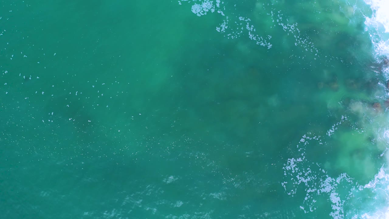 Aerial view of Los Cabos ocean water with a curving foam band over darker submerged shapes, with no visible people.