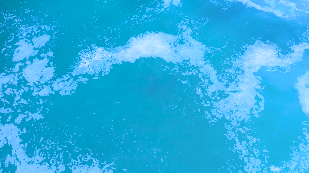 Los Cabos ocean surface seen from above, with white foam gathering along the top and left edges over blue water and no visible people.