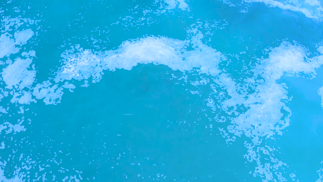 Overhead Los Cabos ocean frame with scattered white foam across bright blue water and no visible people, boats, or shoreline.