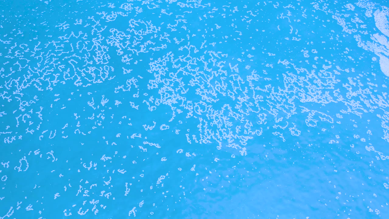 Los Cabos water surface seen from above, with thin white floating marks dispersed over blue water and no visible people.