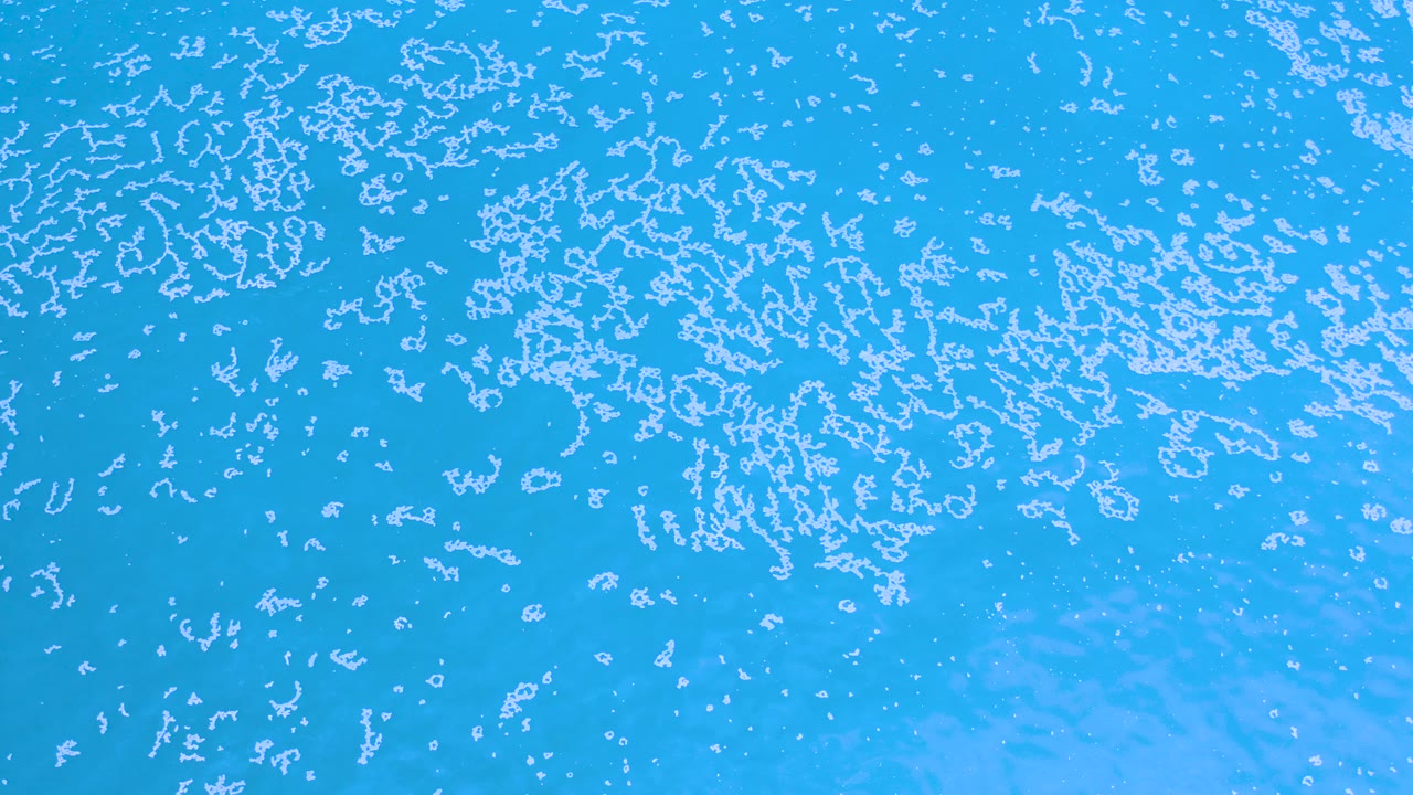 Top-down aerial view of turquoise ocean water in Los Cabos, Mexico, with scattered white sea foam patterns and no visible people.