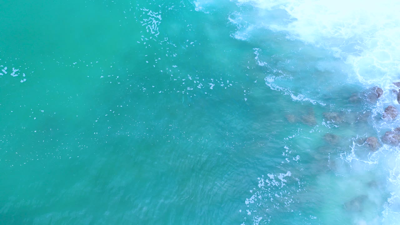 Overhead turquoise surf with foam and rocks at the right edge.