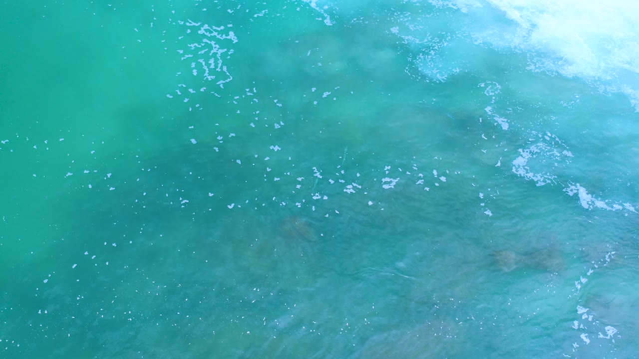Overhead view of turquoise ocean water in Los Cabos, Mexico, with pale foam crossing the upper right and no visible people.