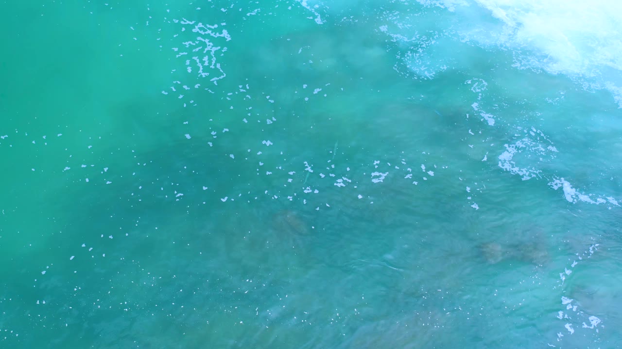 Overhead Los Cabos ocean view with scattered white ripples, blue-green water, faint darker areas below the surface, and no visible people.