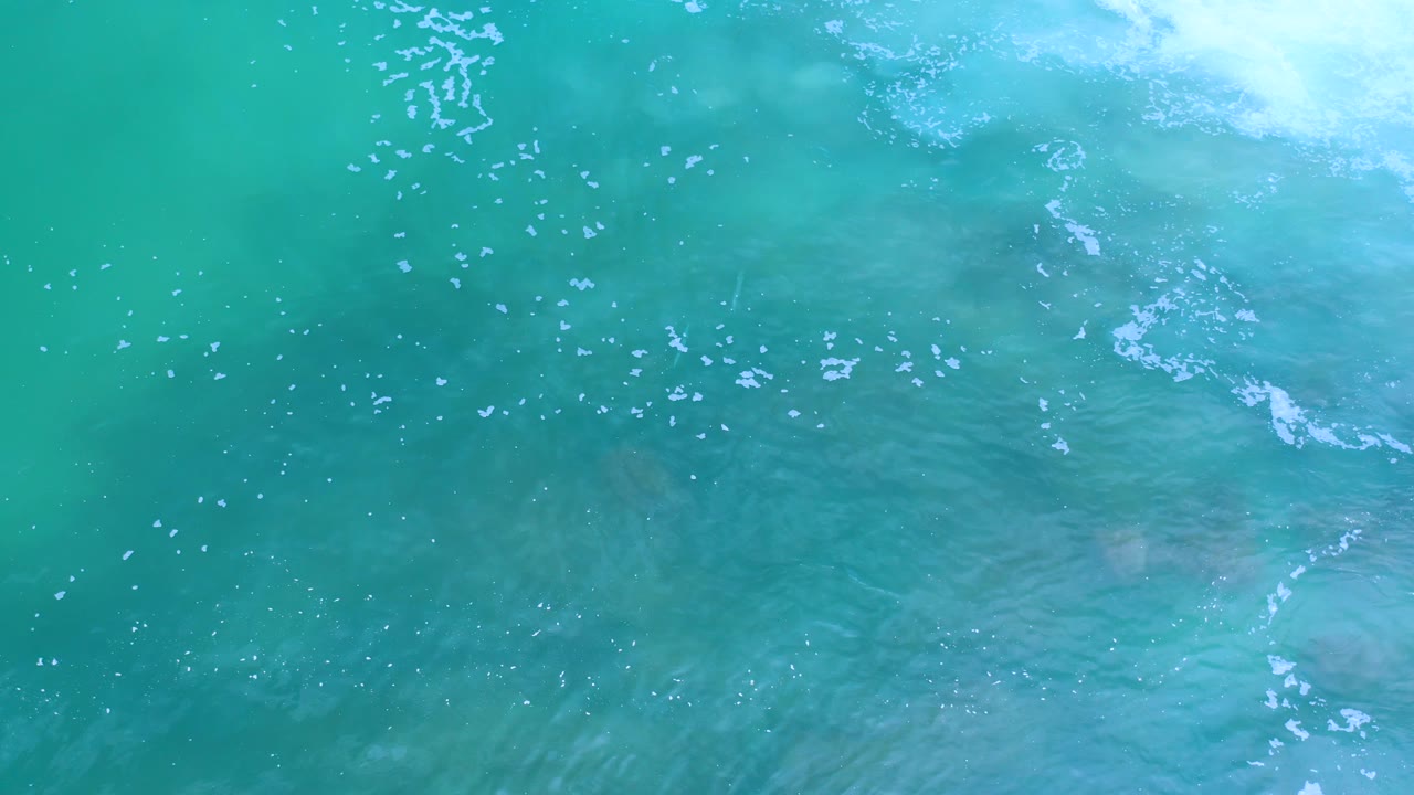 Overhead frame of Los Cabos ocean water with a brighter foam band near the top edge, fine surface ripples, and no visible people.