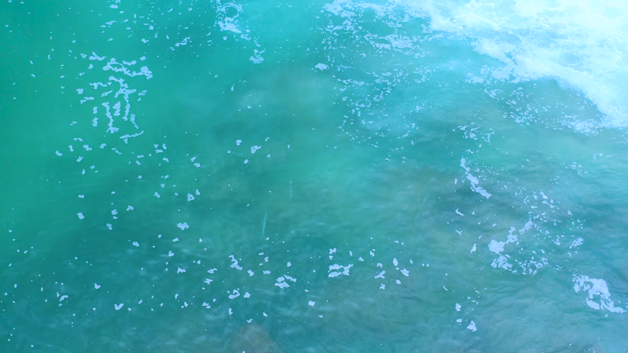 Overhead view of turquoise ocean water in Los Cabos, Mexico, with a pale foam band near the top and no visible people.