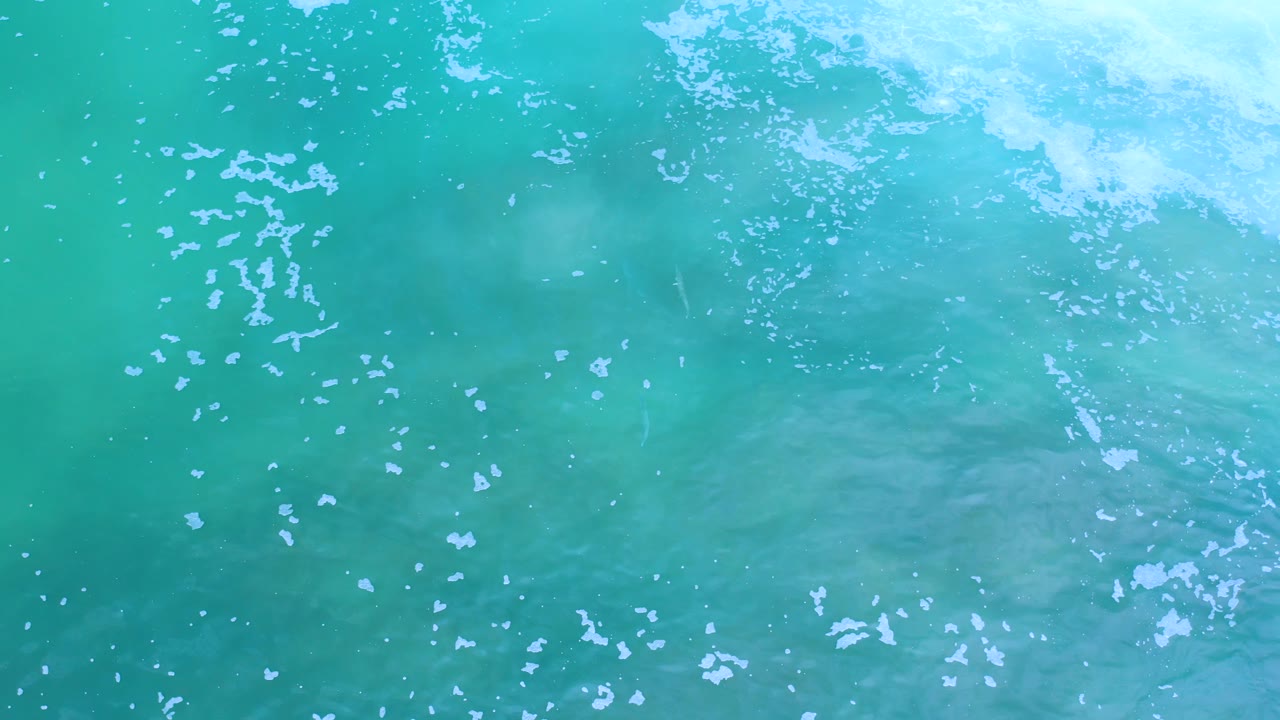 Turquoise water in Los Cabos fills the shot, with light foam near the upper right and faint darker patches under the surface, no visible people.