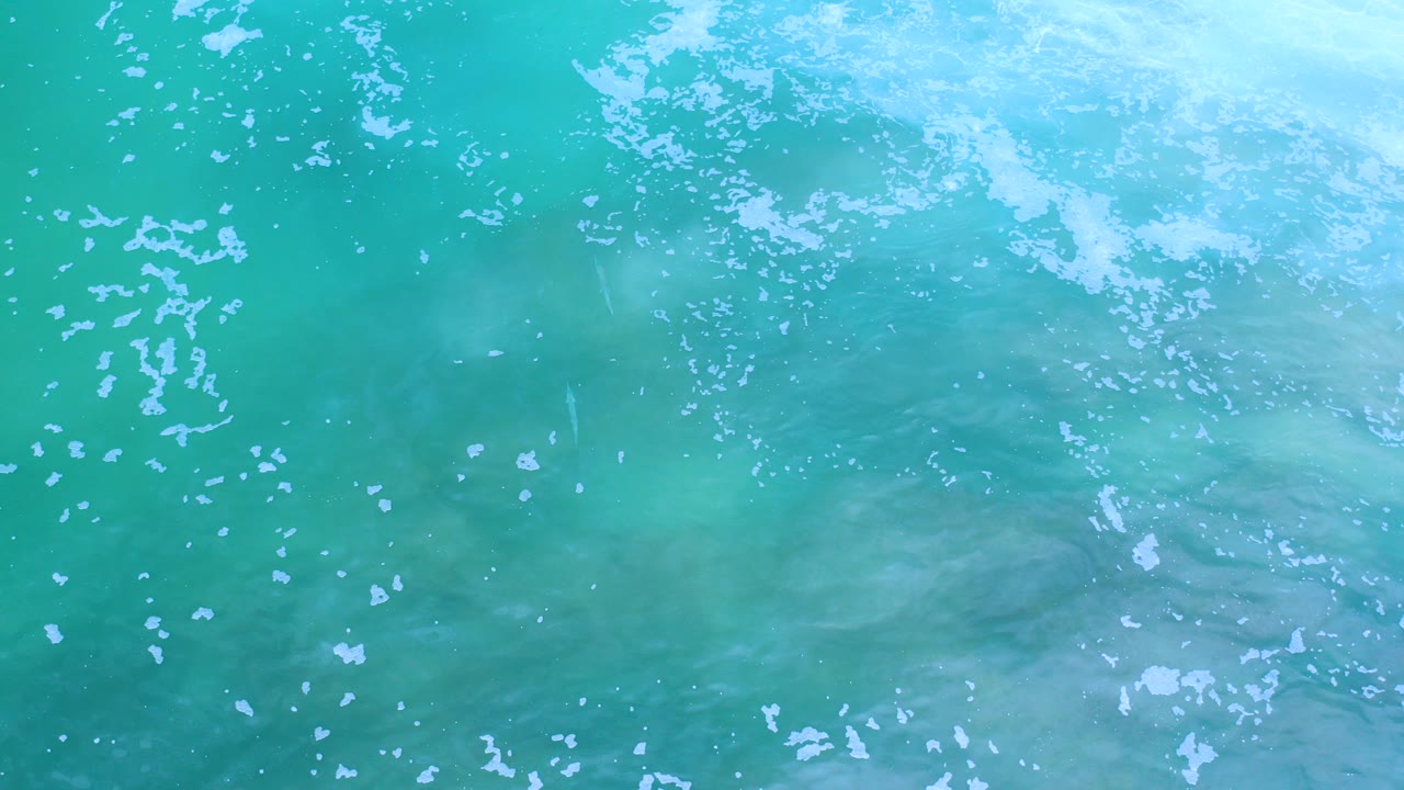 Turquoise ocean water with white foam seen from above.
