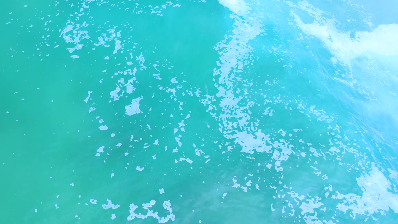 Overhead Los Cabos ocean view with a brighter band of white wave wash along the upper right and no visible people.
