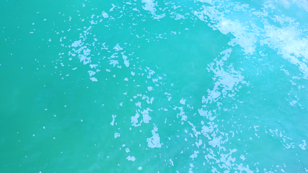 Overhead view of turquoise sea water in Los Cabos, Mexico, with white foam clustered near the upper edge and no visible people.