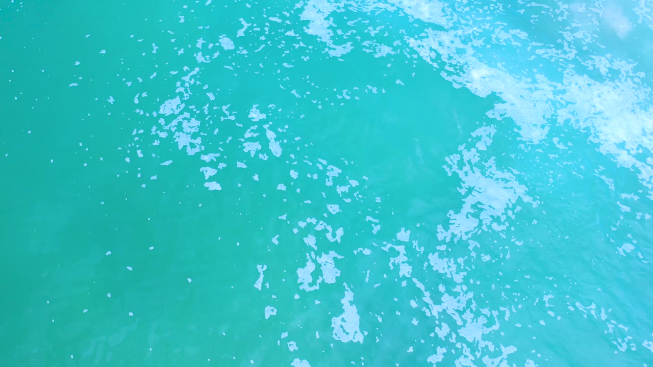 Overhead frame of turquoise water in Los Cabos, Mexico, with broken white foam patterns near the top and right side and no visible people.