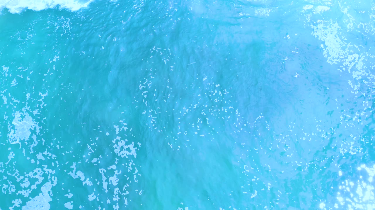 Los Cabos water texture at 0:01, with foam clustered near the lower left and a darker vertical wash pattern through the center, no visible people.