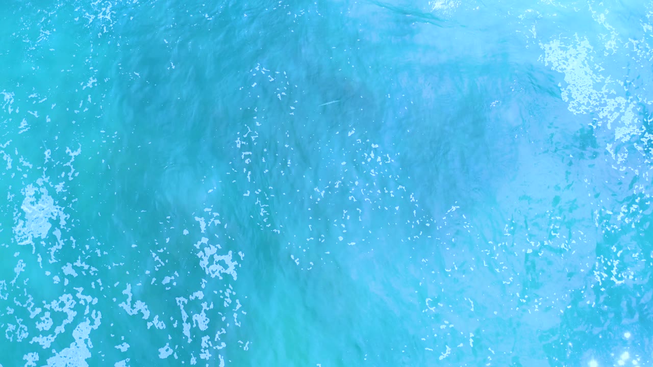 Bright aqua water with scattered white foam and reflective highlights.