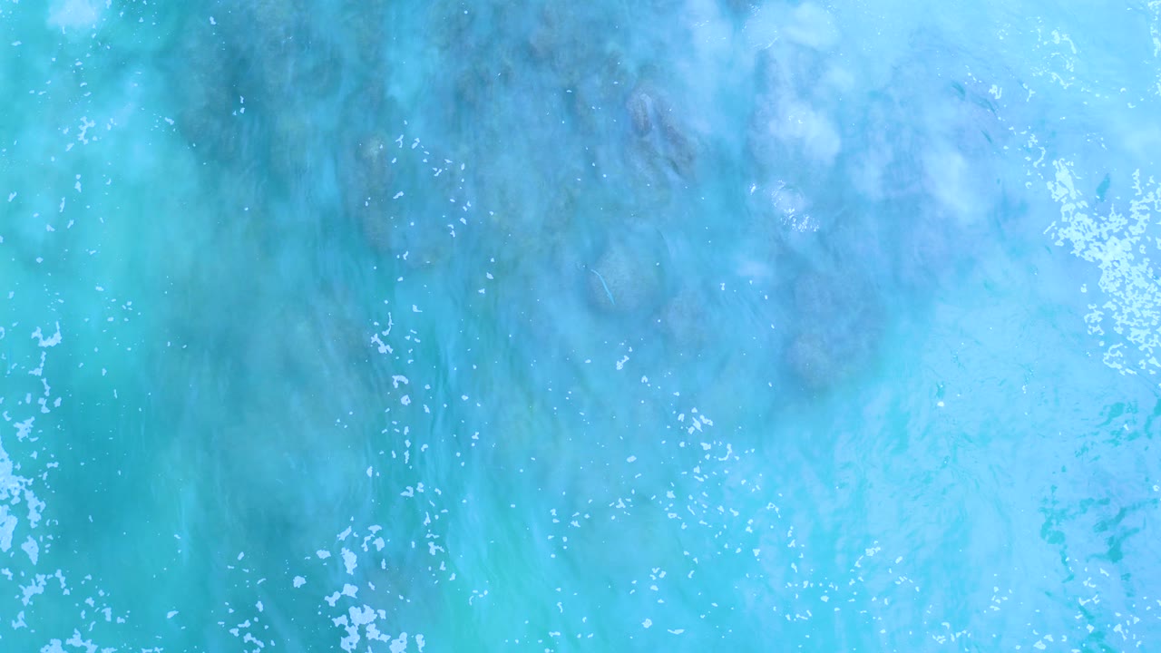 Overhead turquoise seawater in Los Cabos, Mexico, with scattered white foam near the upper edge and no visible people.