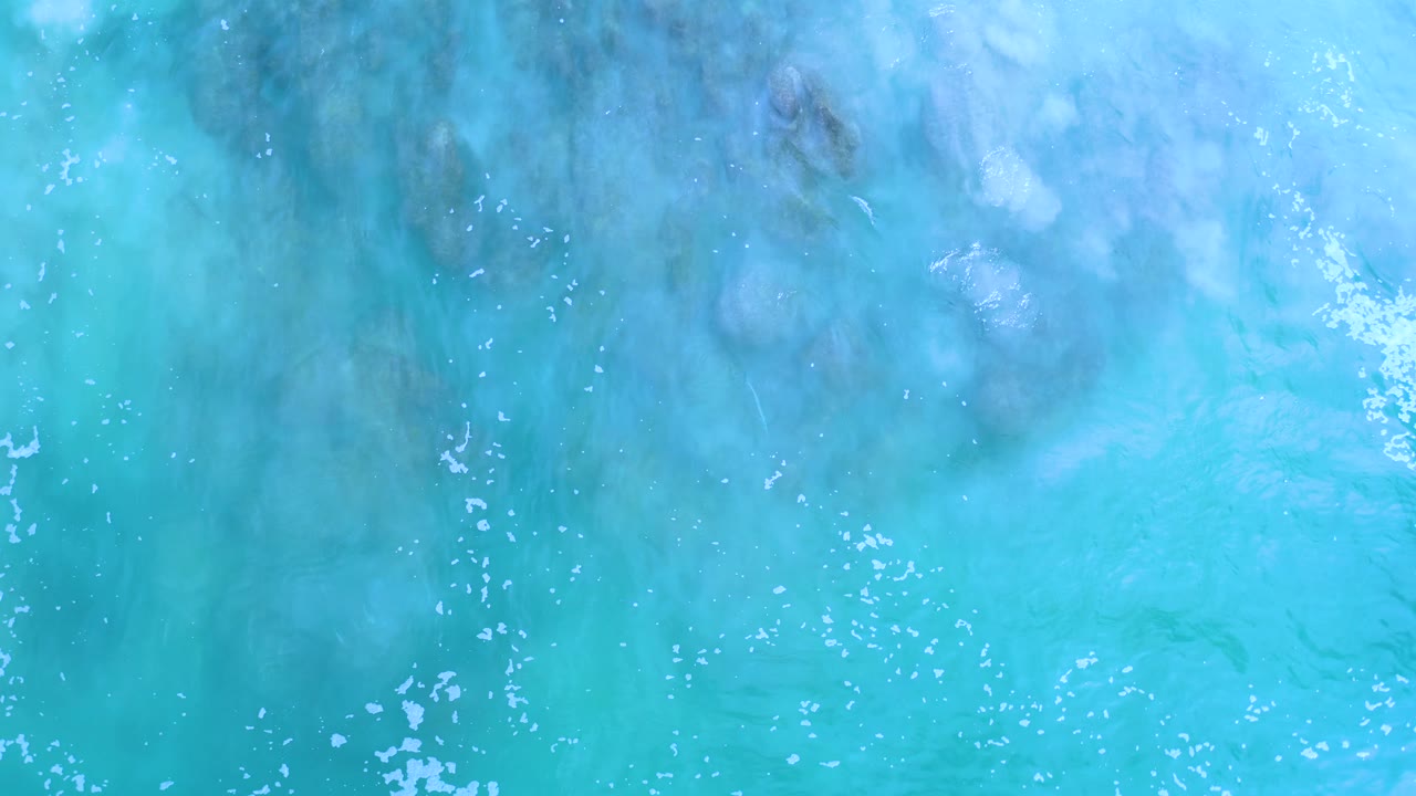 Top-down Los Cabos seawater fills the frame with turquoise color, darker blue patches, and small white foam marks, with no visible people.
