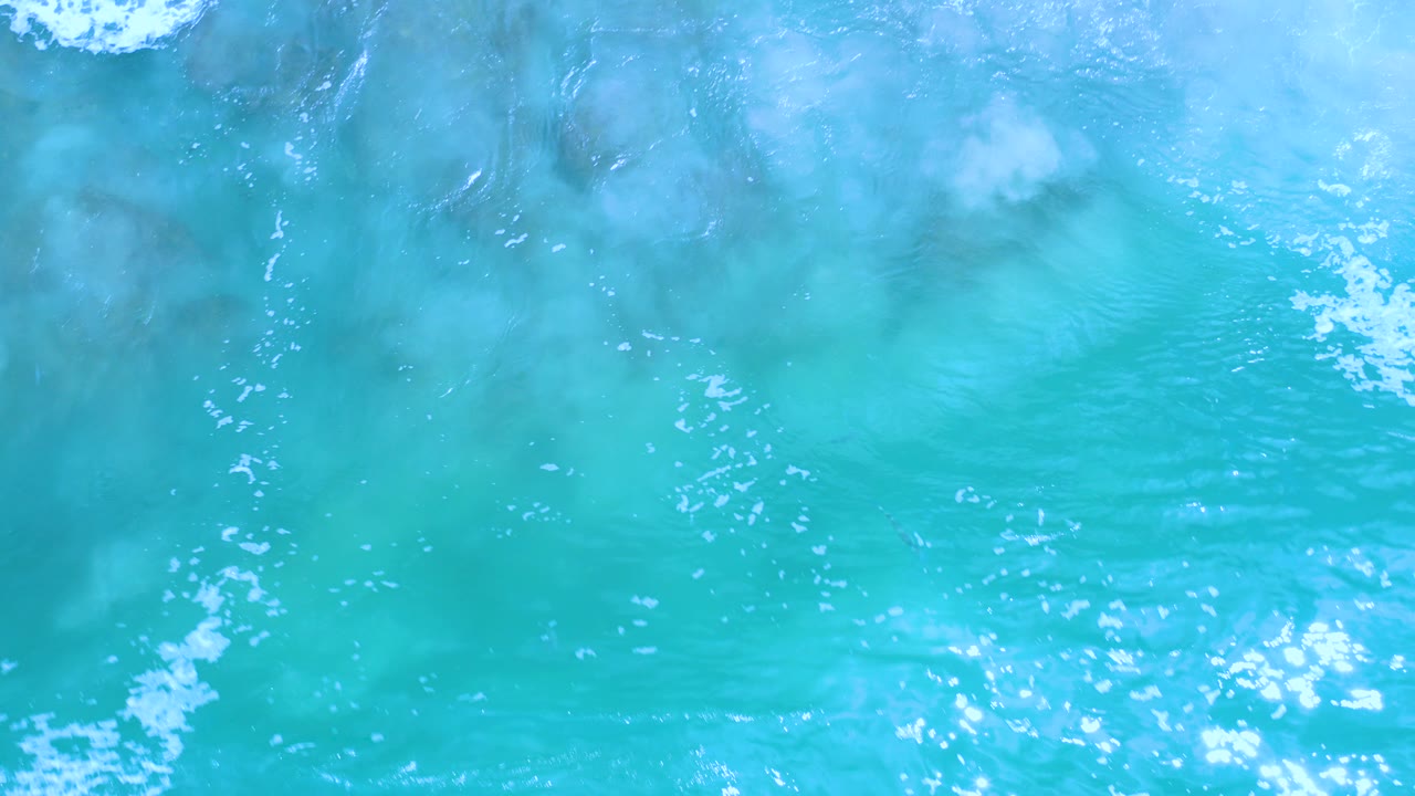 Top-down turquoise seawater with small white wave foam