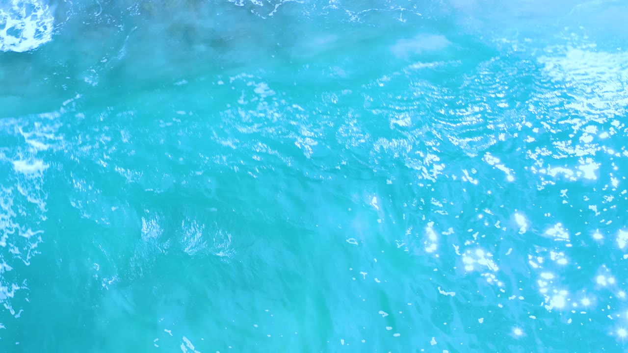 Bright turquoise water in Los Cabos, Mexico, shows stronger sun sparkle and light wave streaks across the surface, with no visible people.