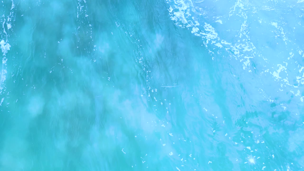 Aqua Los Cabos water shows blurred vertical wave streaks, scattered white highlights, and no visible people.
