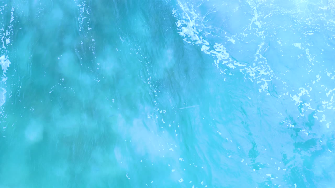 Bright turquoise Los Cabos ocean water fills the frame, with white foam tracing the upper area and no visible people.