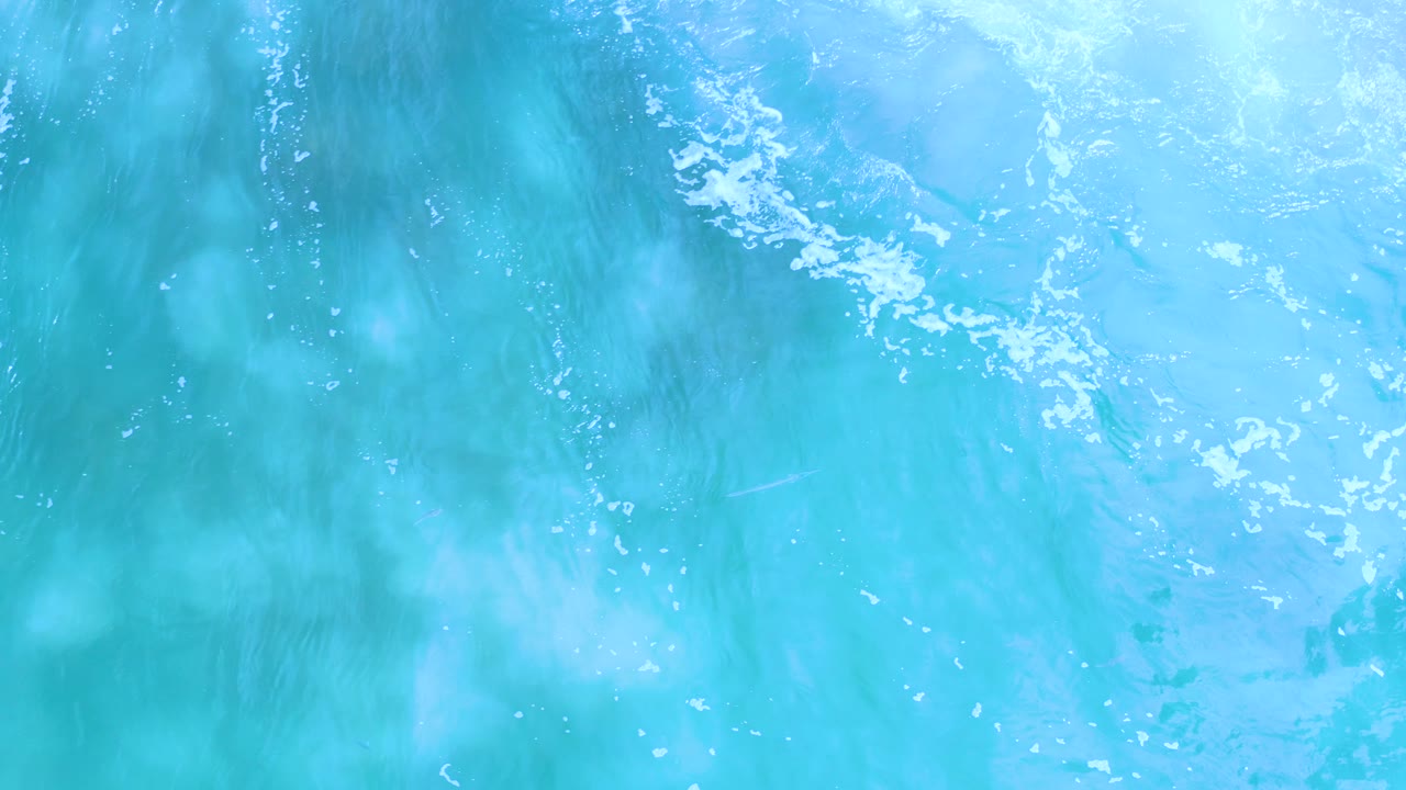 Blue-green Los Cabos ocean water appears denser on the left side, with pale foam across the upper frame and no visible people.