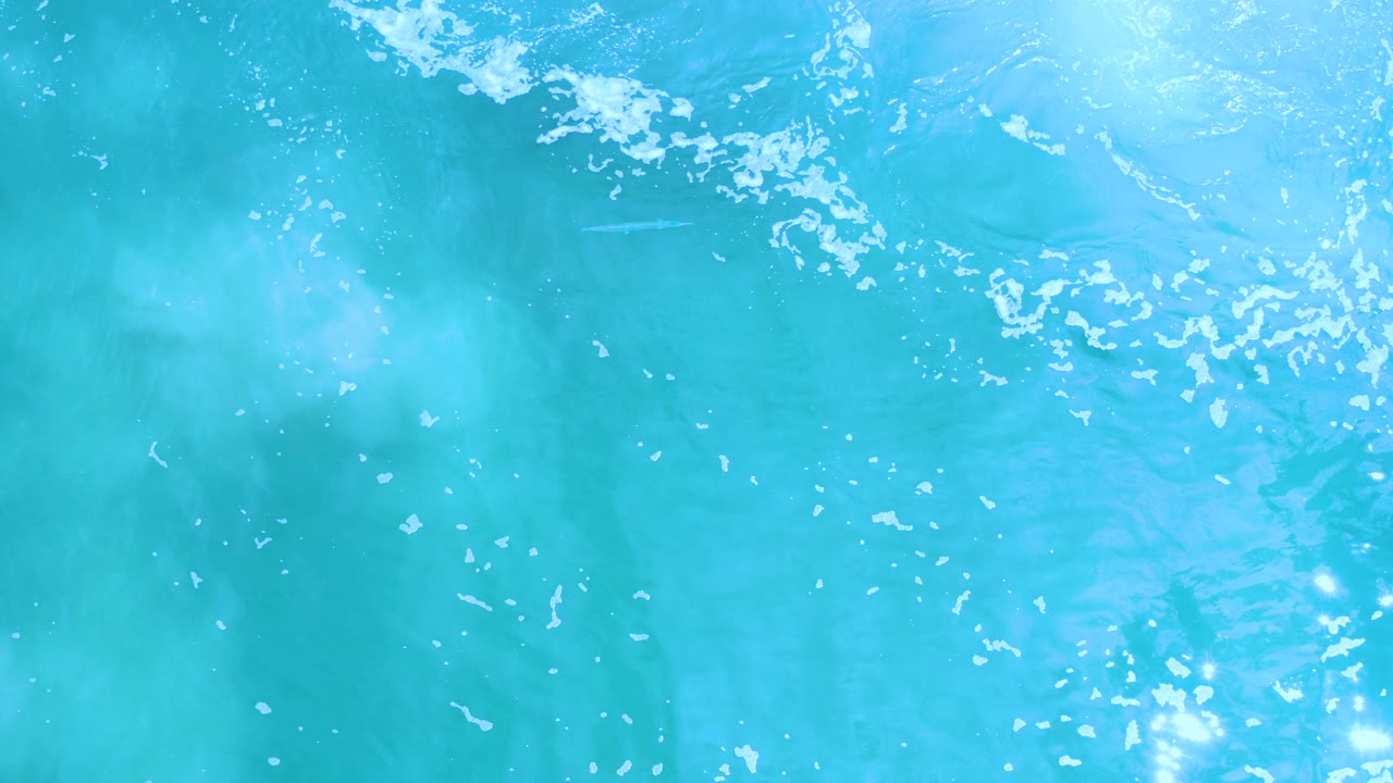 Turquoise ocean water in Los Cabos fills the frame with scattered white foam near the top edge, soft underwater haze, and no visible people.