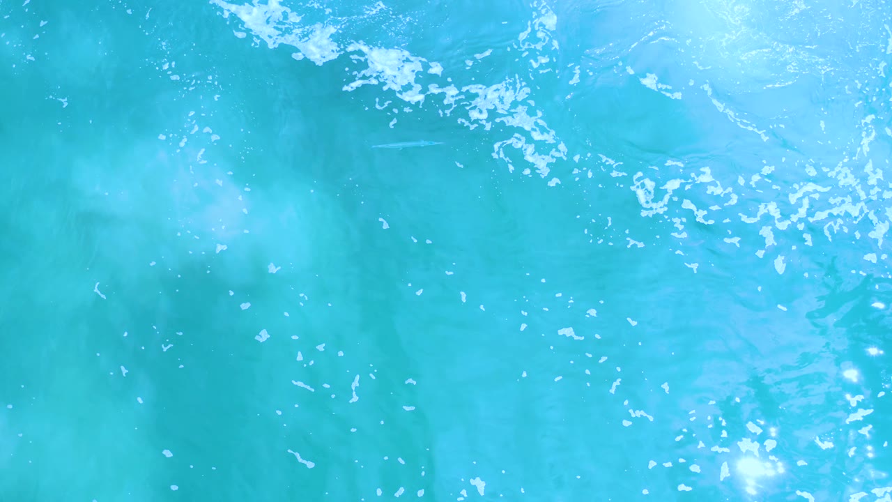 Los Cabos ocean water appears as a bright blue abstract surface with curved ripple lines, small white bubble clusters, and no visible people.