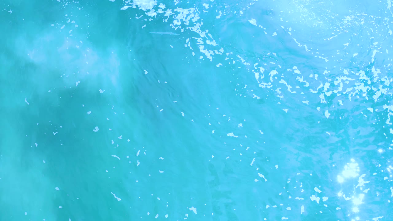 Blue ocean water with bright glare and white bubbles drifting across the surface.