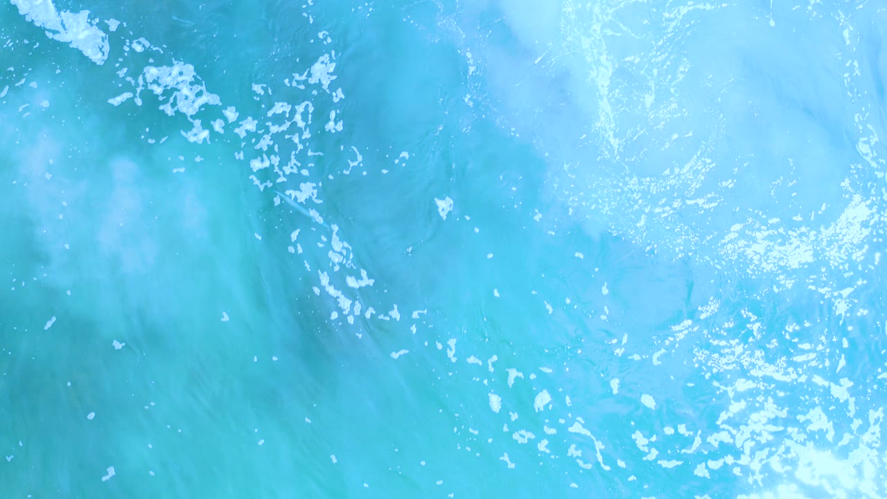 Overhead view of turquoise ocean water in Los Cabos, Mexico, with scattered white foam and no visible people.