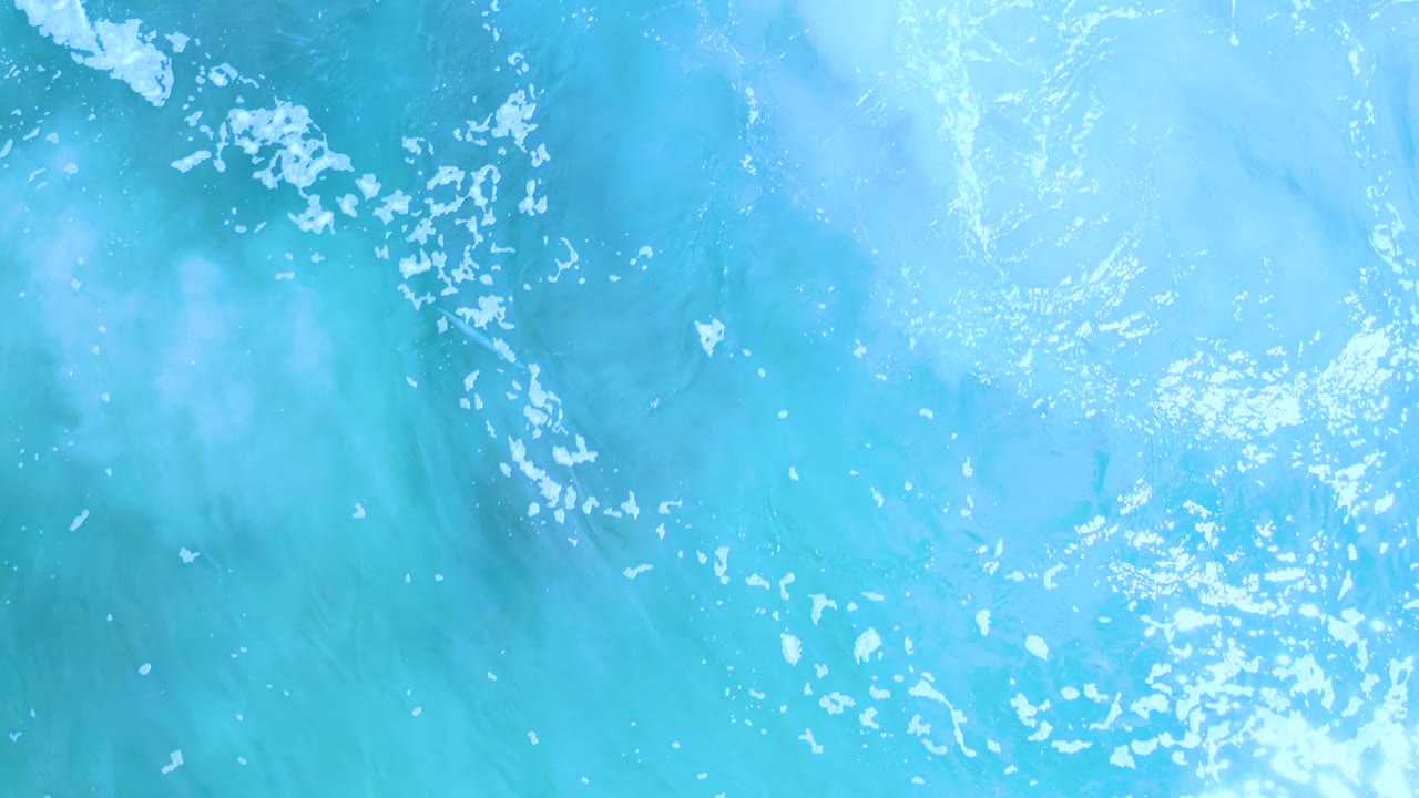 Bright blue-green ocean water in Los Cabos, Mexico, with foam gathered near the upper edge and no visible people.