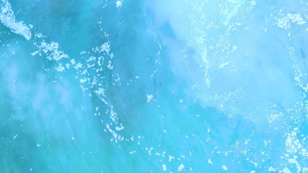 Pale turquoise ocean surface in Los Cabos, Mexico, with small white bubble clusters across the frame and no visible people.
