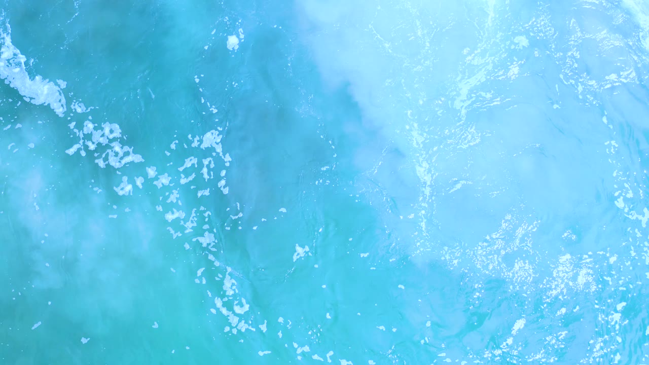 Aqua ocean water in Los Cabos, Mexico, with brighter foam streaks crossing the upper left area and no visible people.