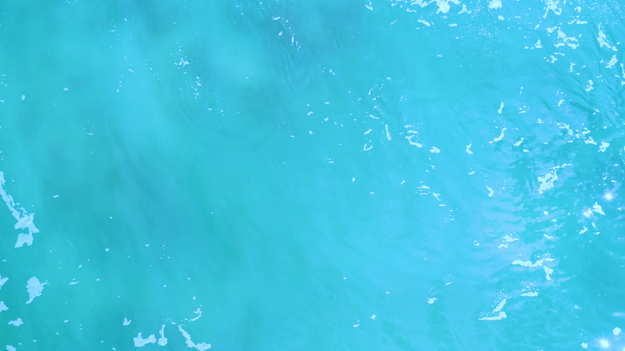 Light blue water surface with sun reflections and faint foam