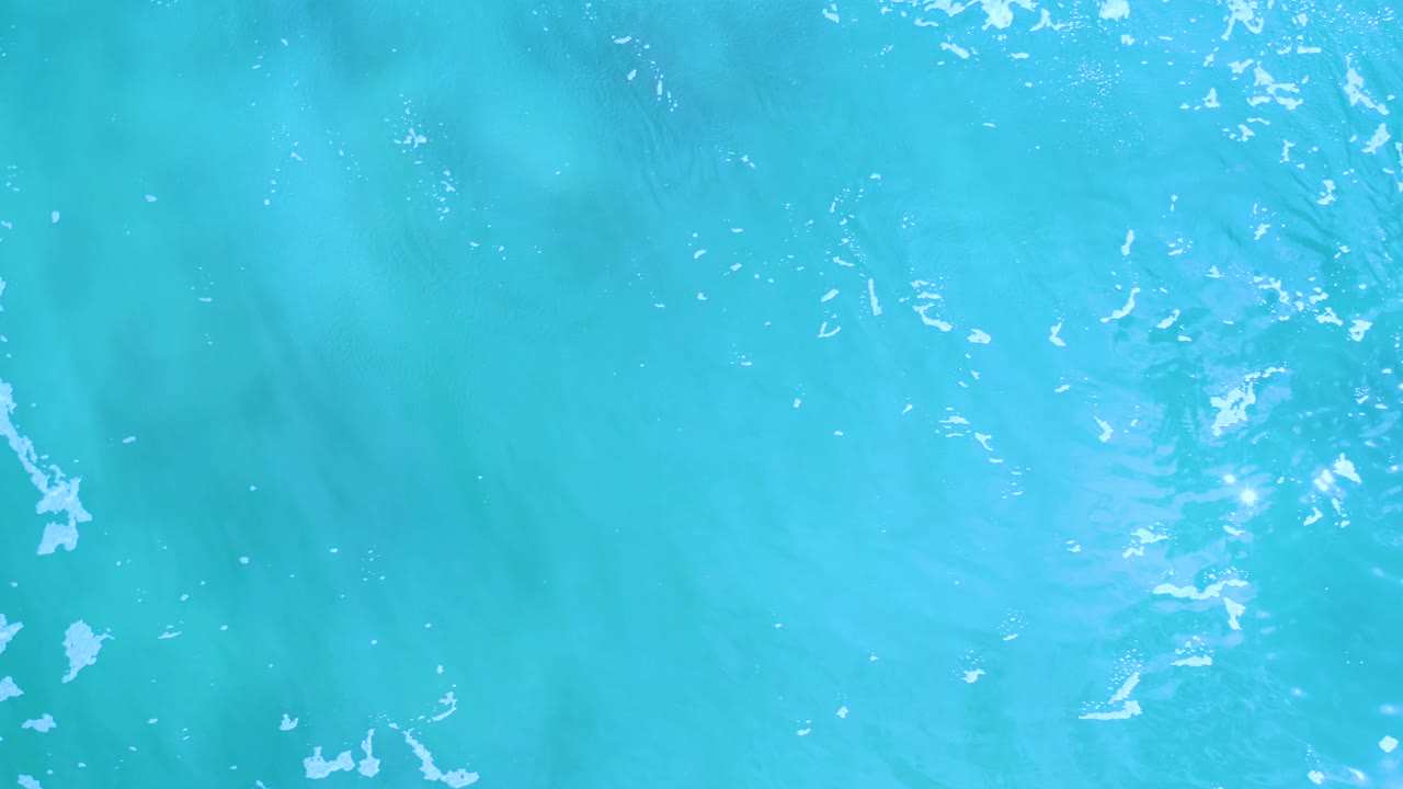 Aerial frame of turquoise water in Los Cabos, Mexico, with scattered white highlights and soft ripples across the surface, with no visible people.