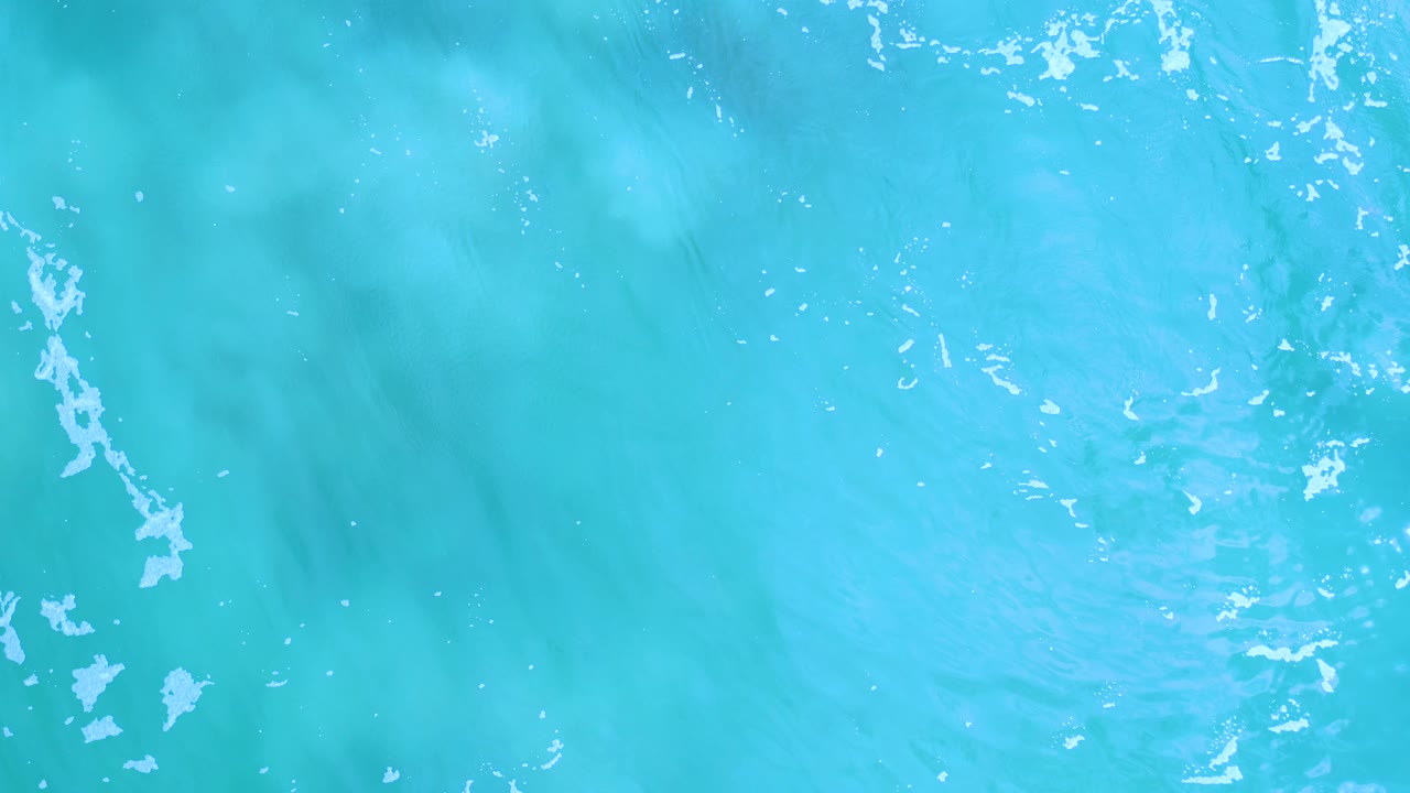 Top-down aquamarine water in Los Cabos, Mexico, with pale foam lines, soft darker patches below the surface, and no visible people.