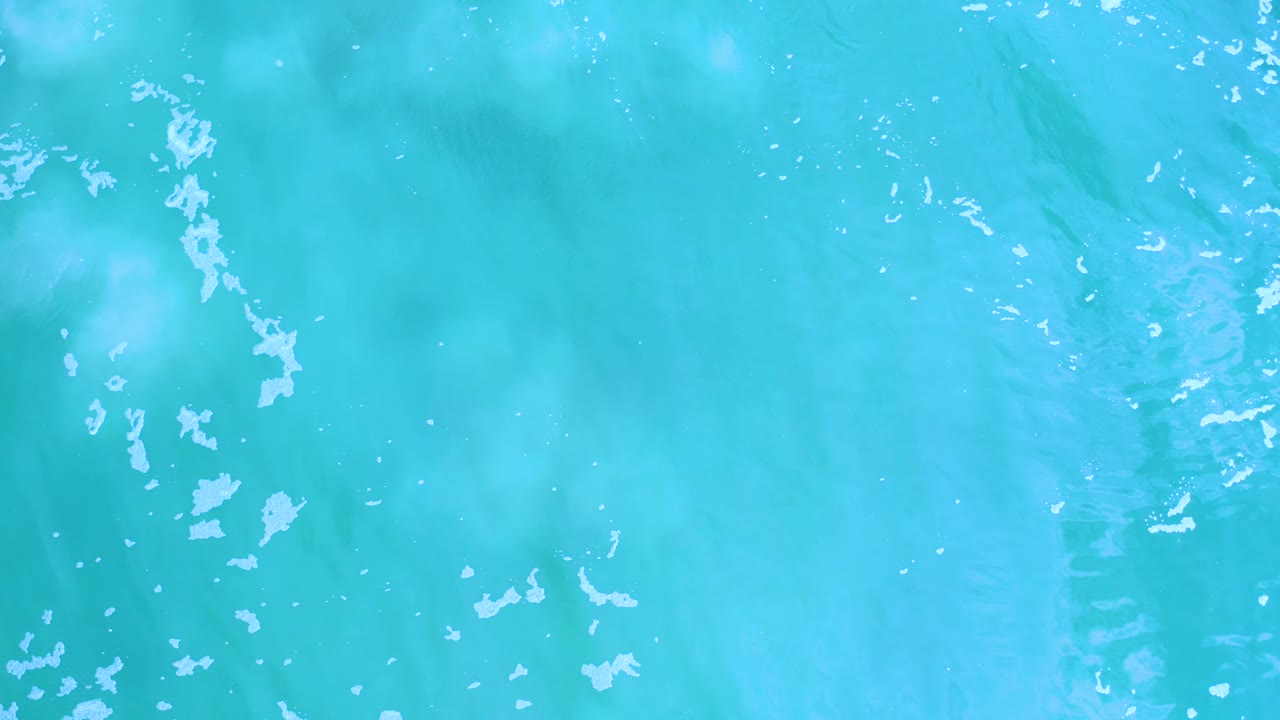 Blue-green water in Los Cabos shows pale foam patches drifting across the surface with no visible people or shoreline.
